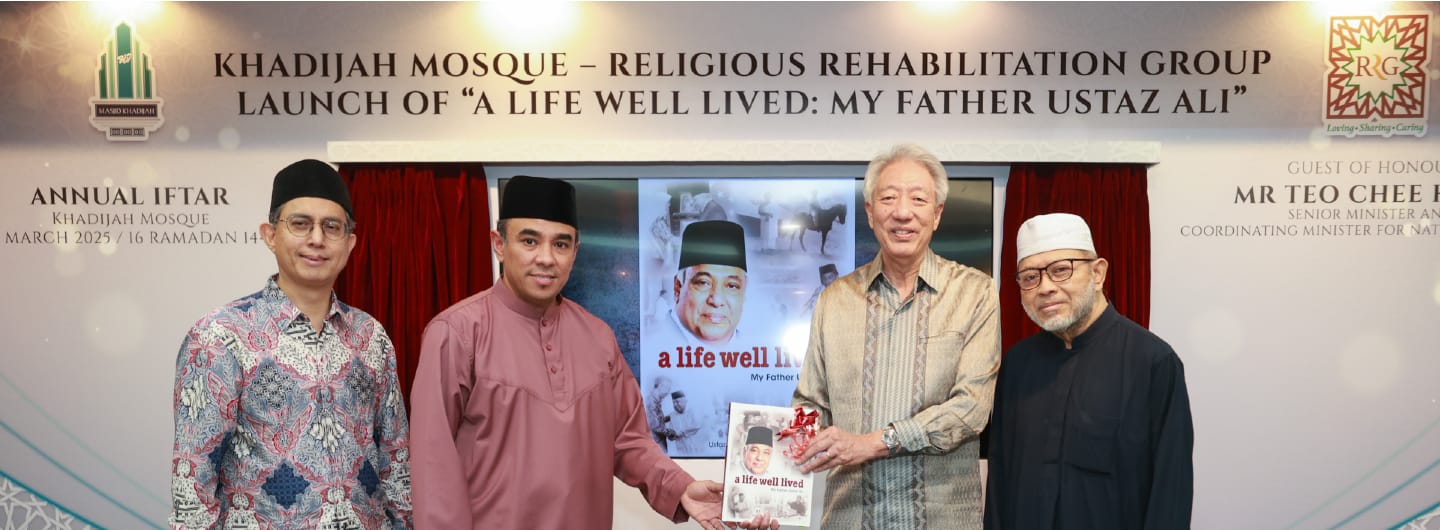 Four men posing with "A Life Well Lived" book launch backdrop at Khadijah Mosque.